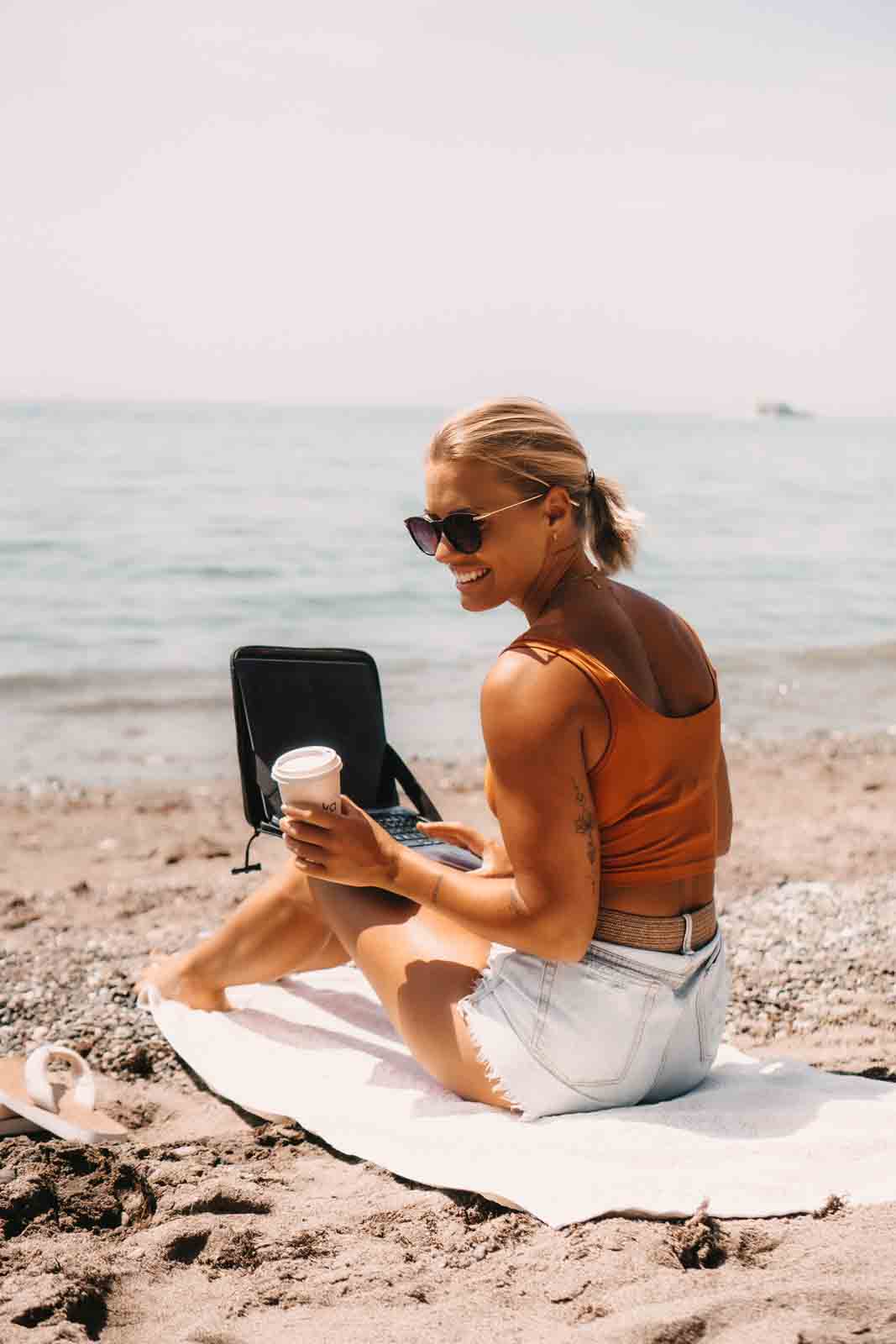 Frau mit wasserdichter Laptop-Tasche am Strand und Notebook als mobile Workstation – ideal für digitales Arbeiten auf Reisen, Outdoor-Abenteuer, Remote Work und den flexiblen Arbeitsplatz am Meer.